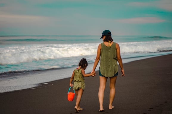 Mother and daughter walking together on the beach, holding hands